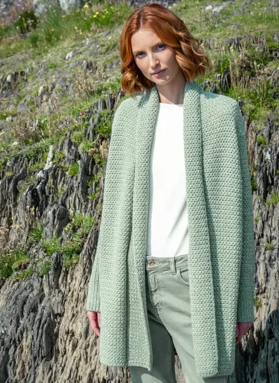 Red headed model standing in rocky area wearing a sage green knitted kilcoole textured coatigan